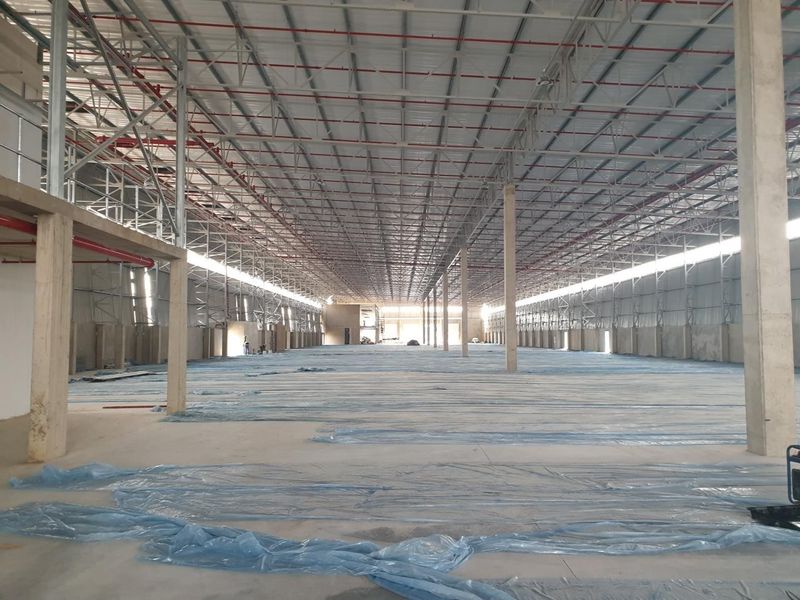 Expansive industrial warehouse space featuring high ceilings with exposed steel trusses, fire sprinkler systems, and durable concrete flooring throughout.