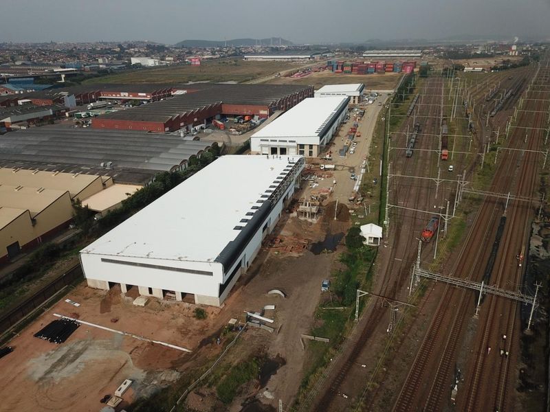 Aerial view of an industrial property featuring large warehouse structures under construction, situated adjacent to active railway lines.