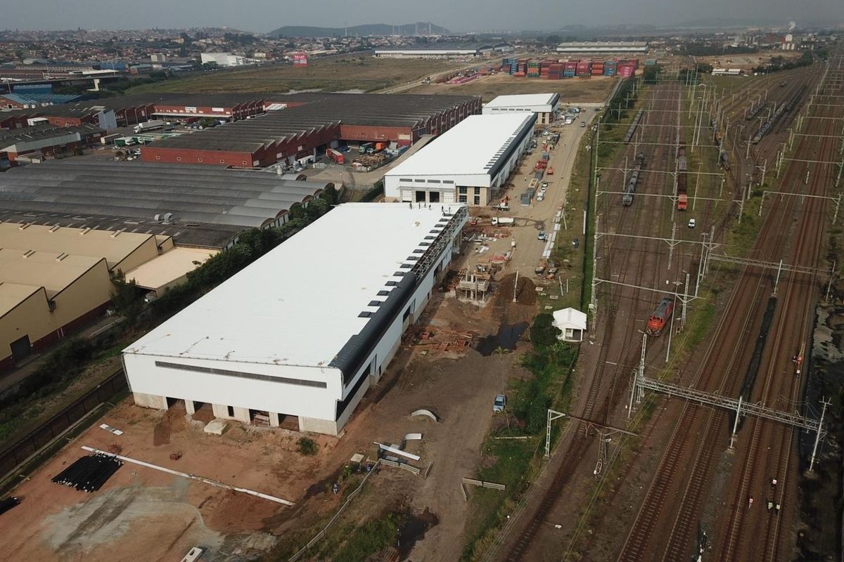 Aerial view of an industrial property featuring large warehouse structures under construction, situated adjacent to active railway lines.