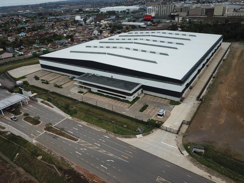 Aerial view of a large industrial warehouse facility featuring a metal roof, dedicated parking area, and secure gated entrance.