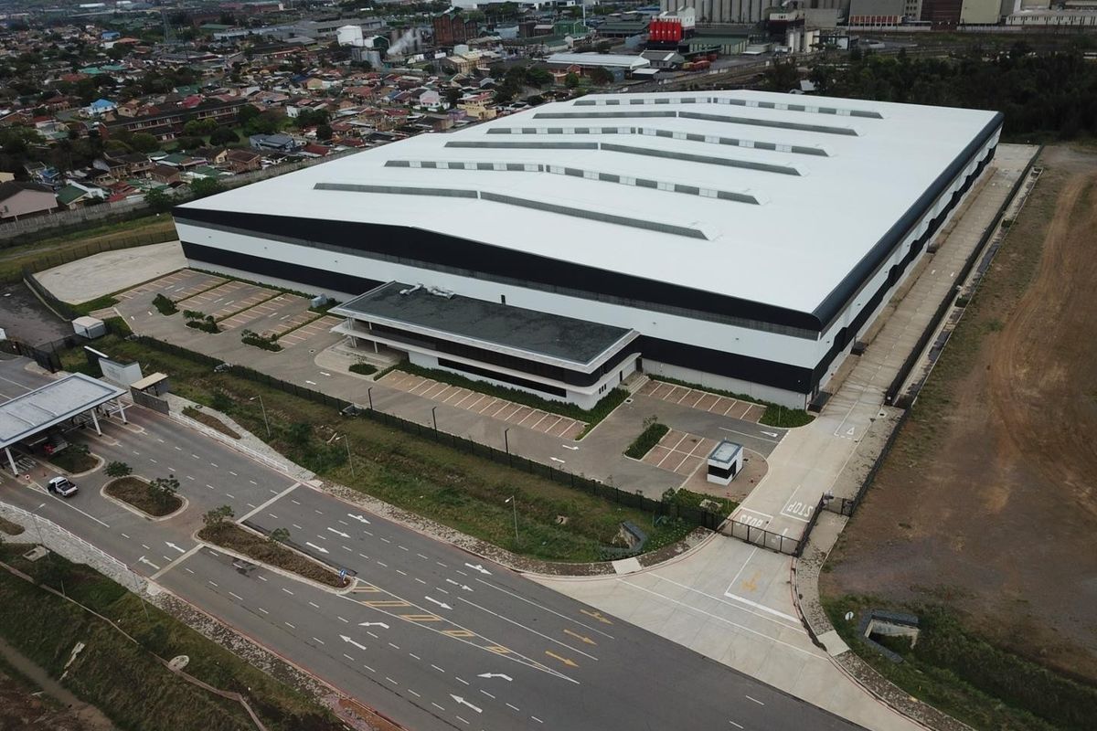 Aerial view of a large industrial warehouse facility featuring a metal roof, dedicated parking area, and secure gated entrance.