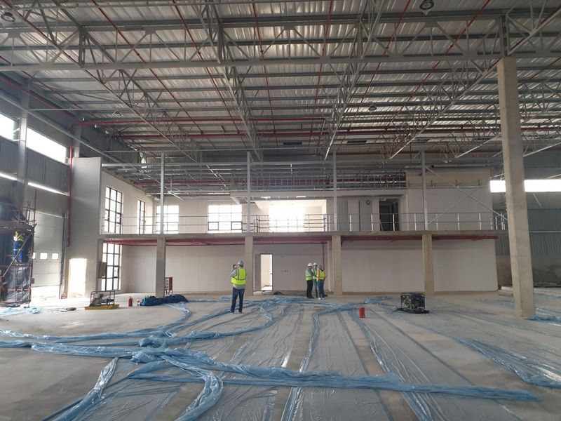 Spacious industrial warehouse interior featuring high ceilings with exposed steel trusses, a mezzanine level, and concrete flooring under construction.