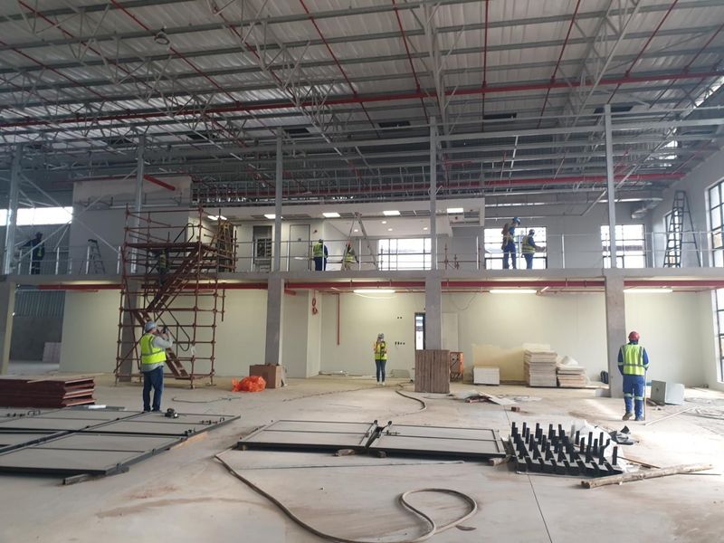 Large industrial warehouse space under construction featuring a steel mezzanine level, exposed roof trusses, and fire sprinkler system.