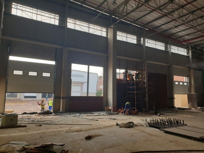 Spacious industrial warehouse interior under construction, featuring high ceilings, concrete flooring, and large roller shutter doors for vehicle access.