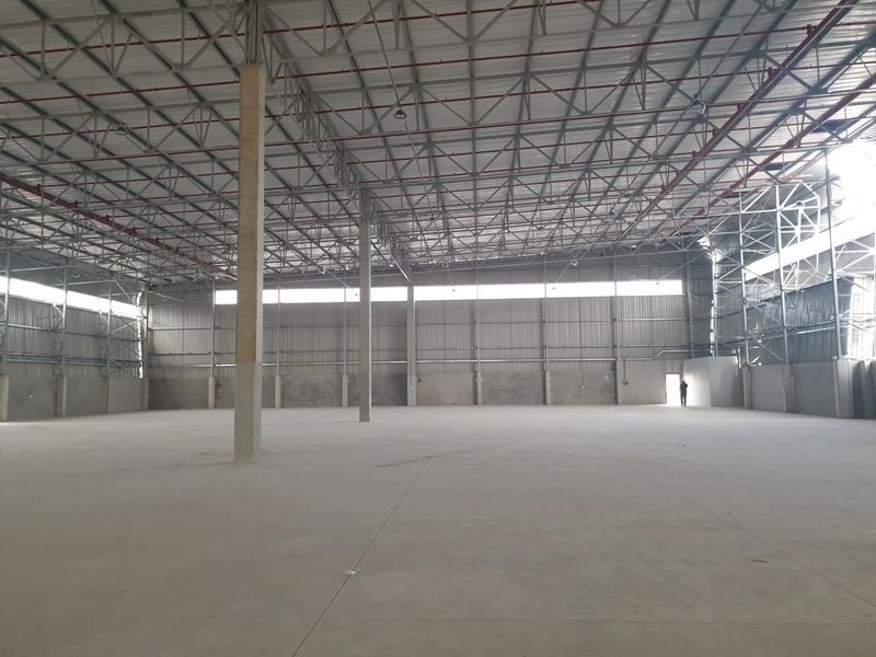Spacious industrial warehouse featuring high ceilings with exposed steel trusses, concrete flooring, and an integrated fire sprinkler system.