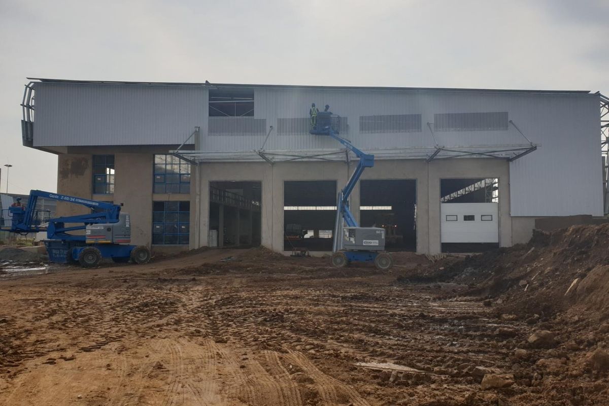 Rear view of an industrial warehouse facility currently undergoing construction and exterior cladding installation with significant site groundworks in progress.