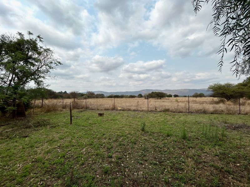 A wide-angle view of the farm landscape featuring open fields, natural vegetation, and distant mountain ranges enclosed by wire mesh fencing.