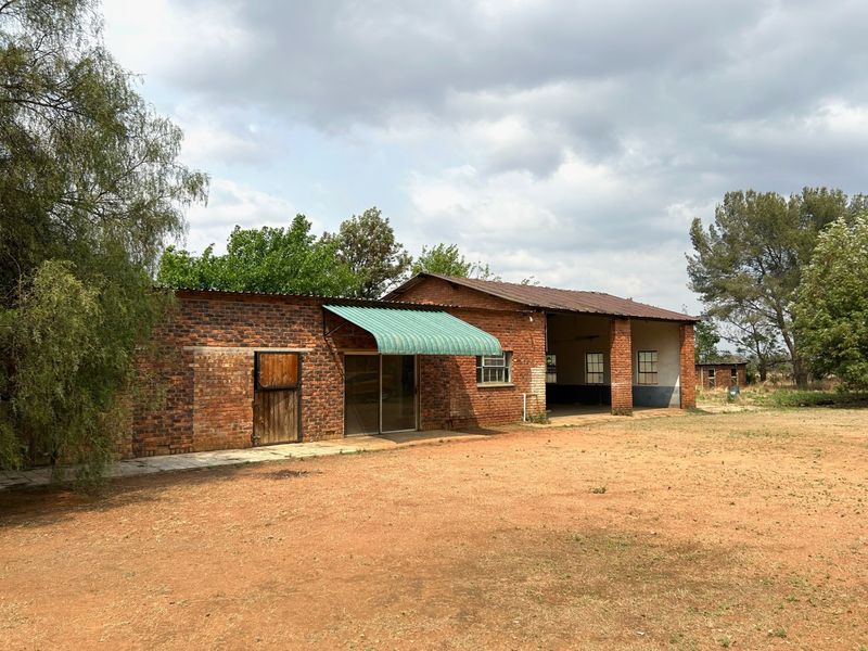 Exterior view of a rustic farm building featuring exposed brick walls, a corrugated metal roof, and an open-sided barn section.
