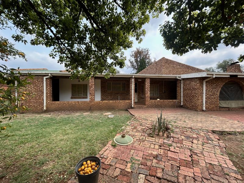 Rear view of a face brick farmhouse featuring a covered patio area and extensive brick paving in the garden.