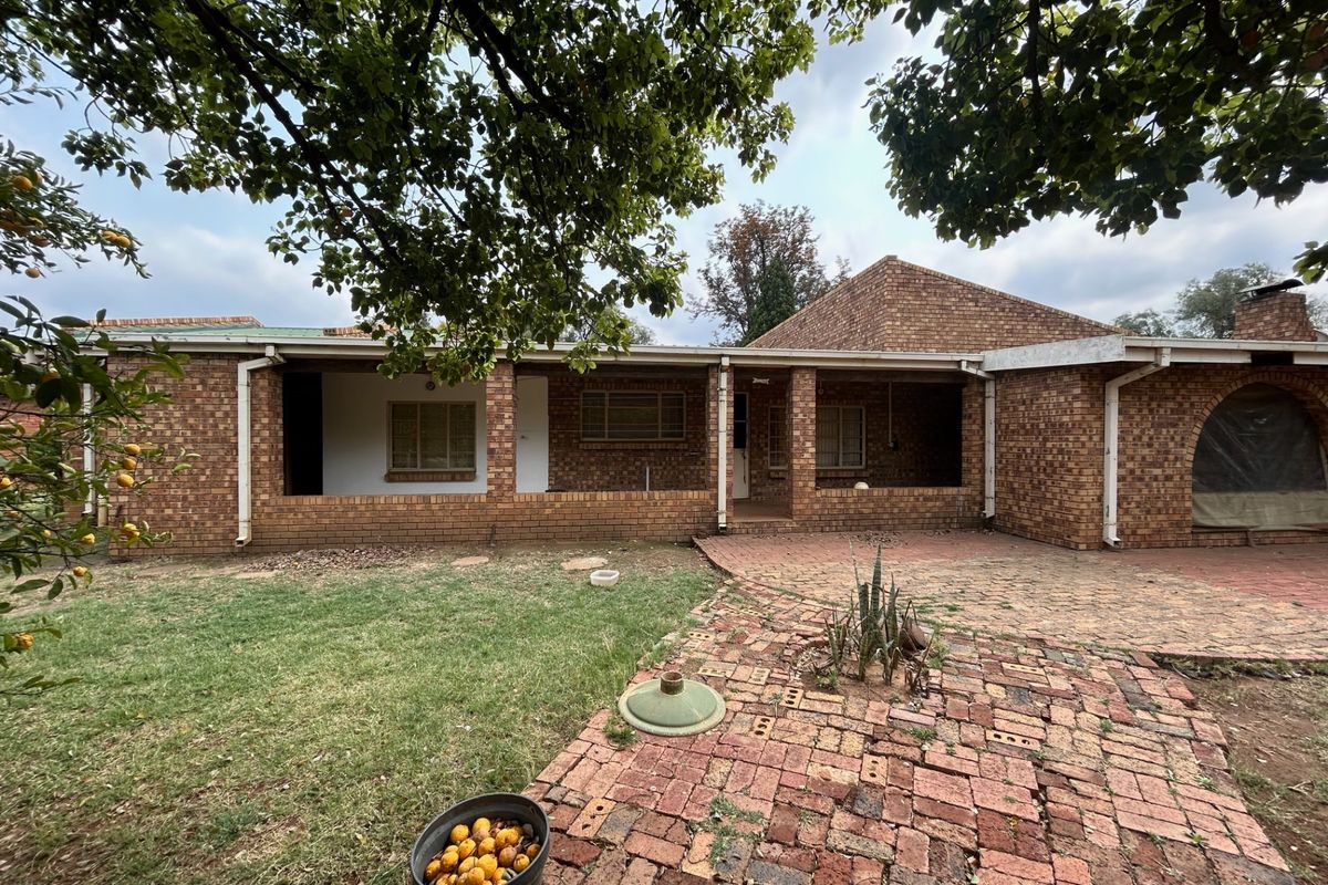 Rear view of a face brick farmhouse featuring a covered patio area and extensive brick paving in the garden.