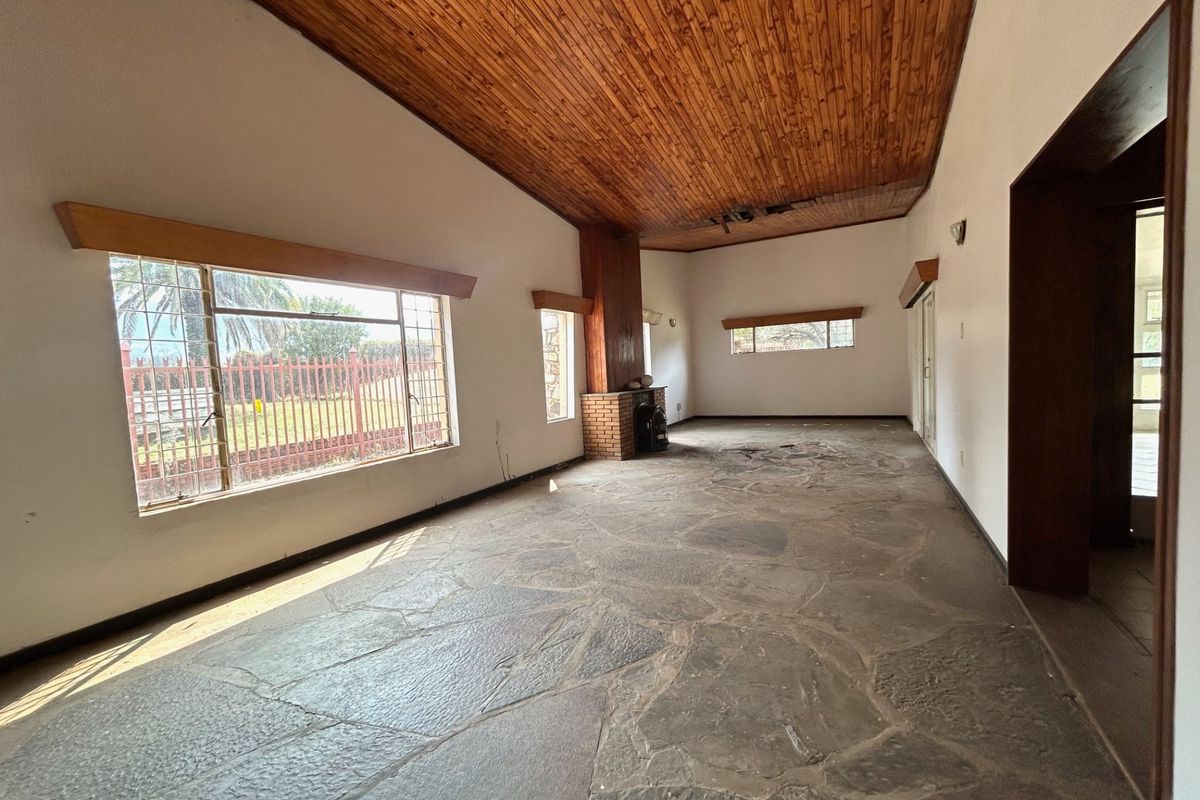 Spacious living area featuring a timber-clad vaulted ceiling, rustic stone flagstone flooring, and a central brick fireplace, offering a blank canvas for renovation.