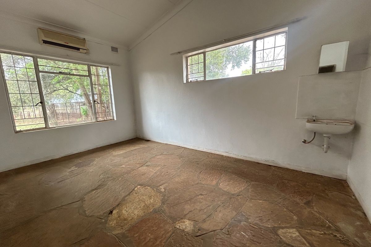An empty bedroom featuring rustic stone flooring, steel-framed windows, a wall-mounted air conditioning unit, and a basic wall-mounted basin.
