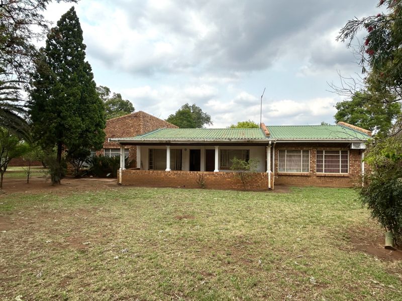 Rear view of a face brick farmhouse featuring a covered patio, corrugated metal roof, and established garden surroundings.