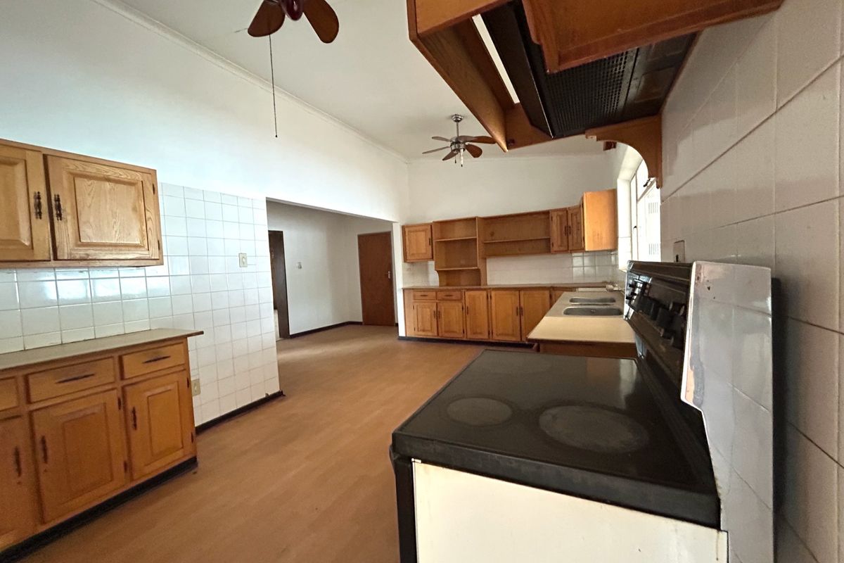 Spacious kitchen featuring wooden cabinetry, tiled splashbacks, and a built-in stove with extractor fan, offering a functional layout with ample storage space.