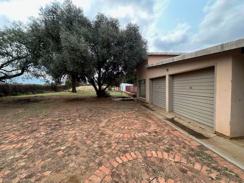 Rear view of the property featuring a double garage with brick paved driveway and mature trees in the garden area.