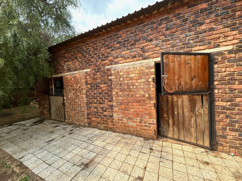 Exterior view of a rustic farm outbuilding featuring exposed brick walls, stable-style wooden doors, and a paved patio area.