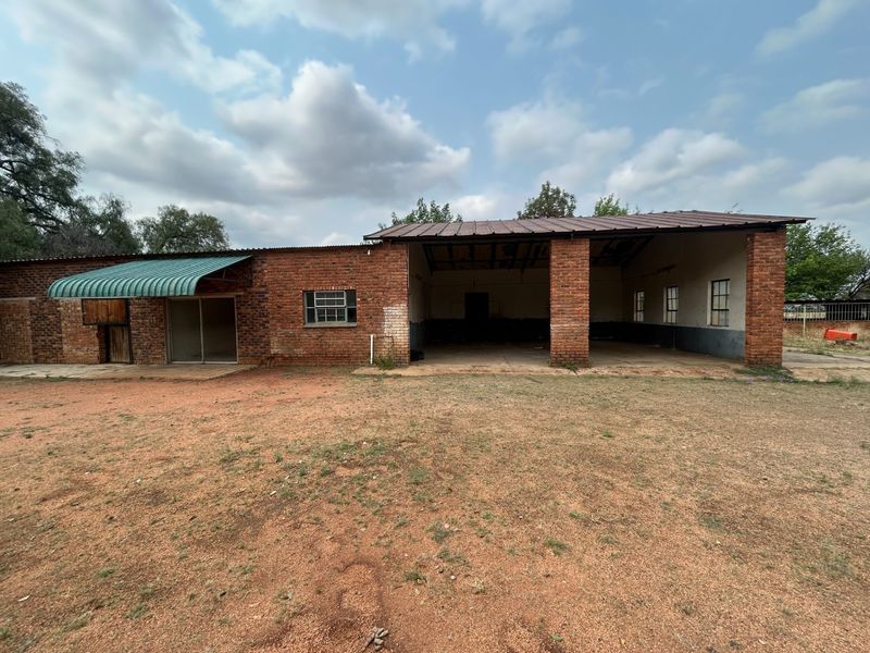 Rear view of a rustic farm building featuring an open-sided barn area, exposed brick construction, and a corrugated metal roof.