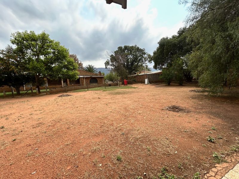 A spacious rear yard area featuring mature trees, perimeter fencing, and a view of the brick-built farm dwelling.