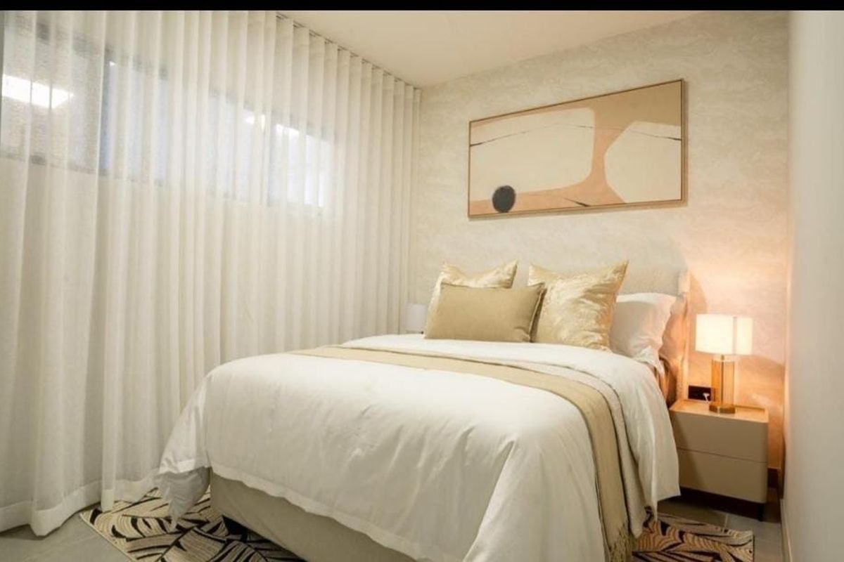 A well-lit bedroom featuring neutral wall finishes, floor-to-ceiling curtains, and integrated electrical fixtures, creating a comfortable and modern living space.