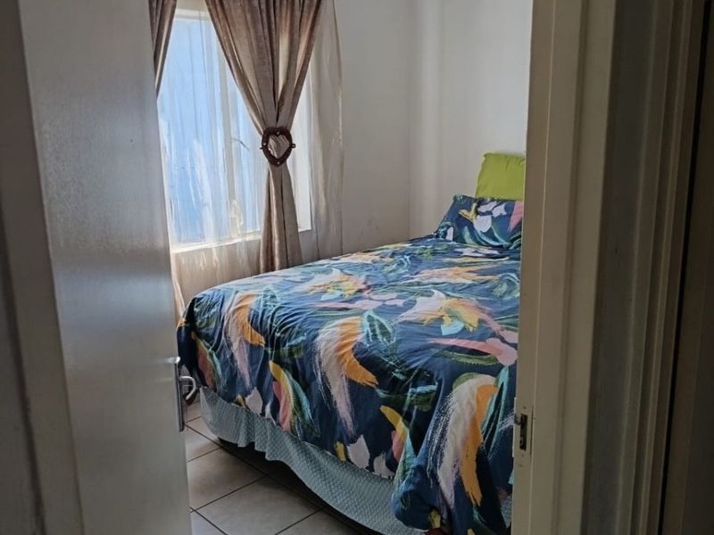 A compact bedroom featuring tiled flooring and a window with curtains, viewed from the doorway.