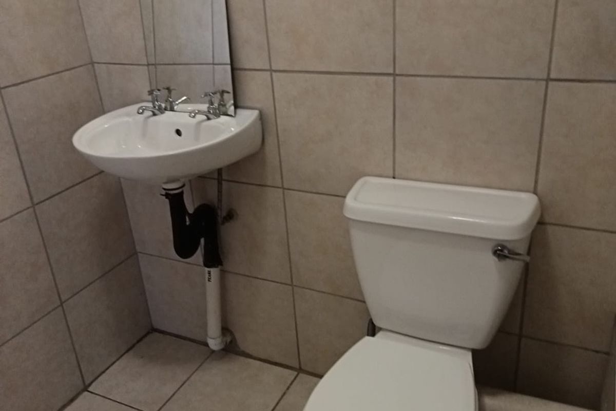 A compact bathroom featuring a wall-mounted basin and toilet with neutral ceramic tiling throughout.