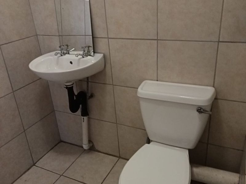 A compact bathroom featuring a wall-mounted basin and toilet with neutral ceramic tiling throughout.