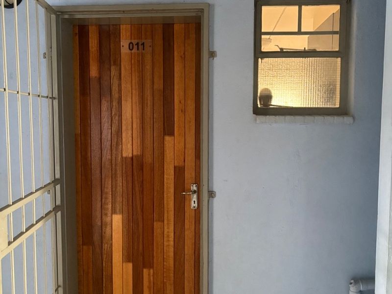 Apartment entrance featuring a wooden door, security gate, and a small window with textured glass.