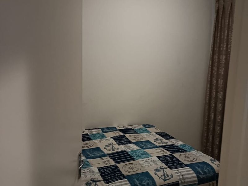 A compact bedroom featuring a ceiling light fixture and window curtain track, viewed from the doorway.