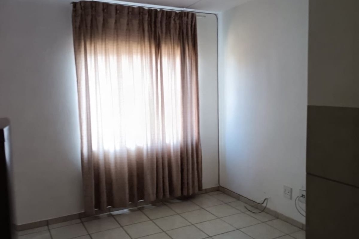 An empty living area featuring neutral tiled flooring and a window with curtains, providing a blank canvas for interior design.