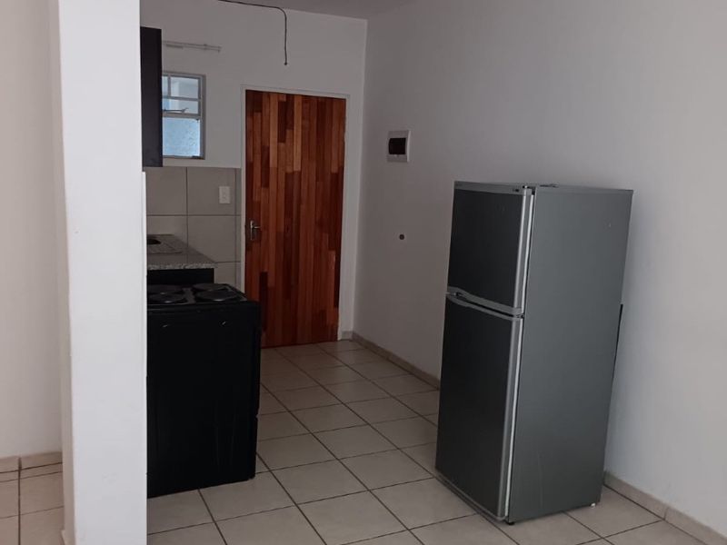 A functional kitchen area featuring tiled flooring, a wooden door, and basic cabinetry, offering a clean and simple space ready for personalization.