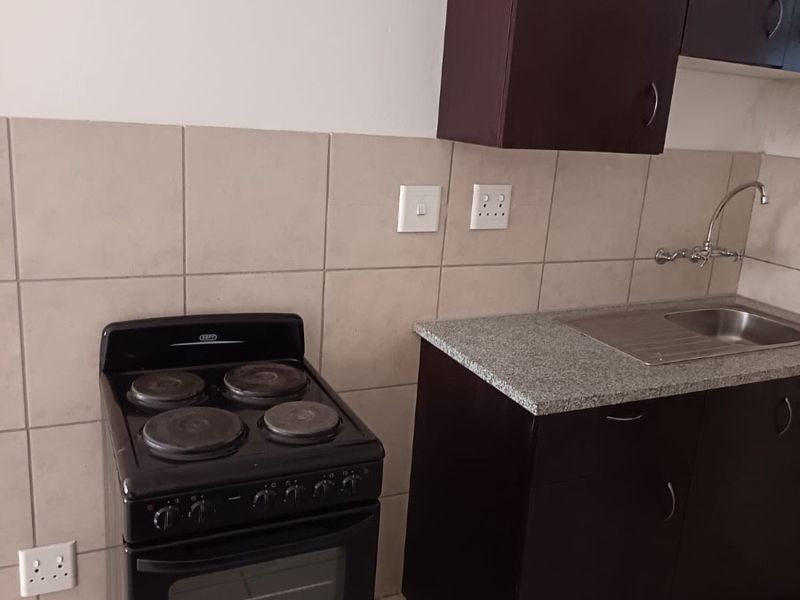 A functional kitchen area featuring dark cabinetry, a stainless steel sink, tiled backsplash, and a freestanding stove.