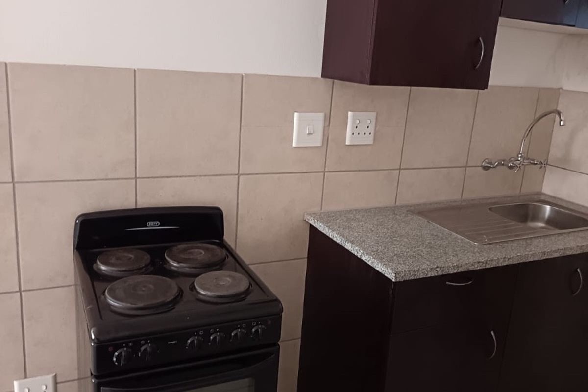 A functional kitchen area featuring dark cabinetry, a stainless steel sink, tiled backsplash, and a freestanding stove.