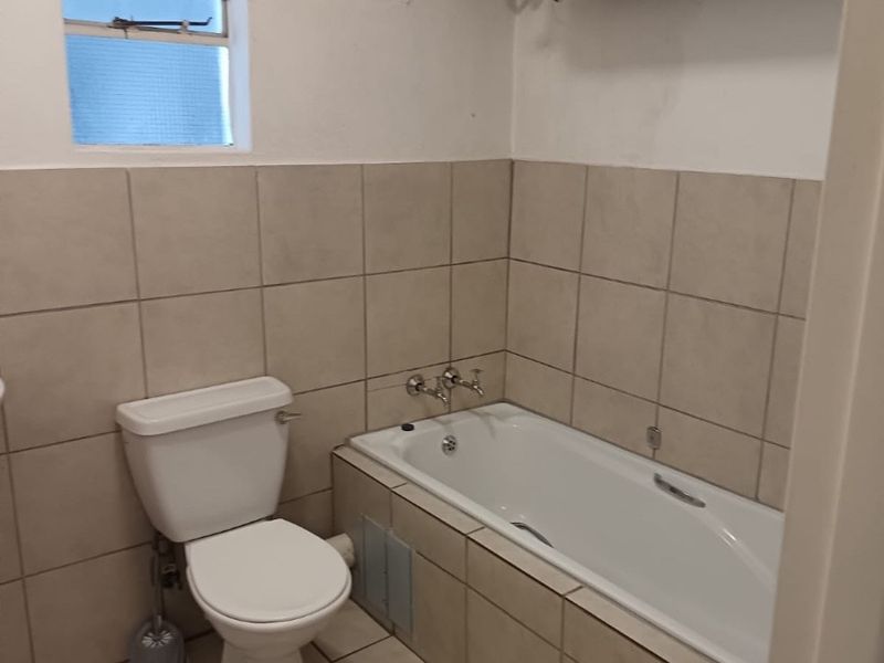 A functional bathroom featuring a bathtub, toilet, and wall-mounted water heater, finished with neutral wall and floor tiles.