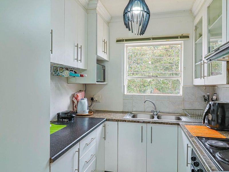 A functional kitchen featuring white cabinetry, laminate countertops, a double bowl sink, and an integrated electric hob with an extractor fan.