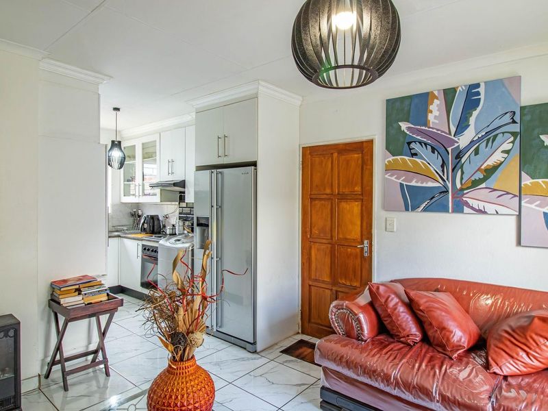 Open-plan living area featuring tiled flooring, coving, and a compact kitchen with built-in cabinetry and an extractor fan.