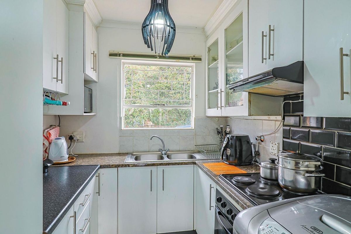 Compact kitchen featuring white cabinetry, dark tiled backsplash, laminate countertops, and integrated cooking appliances, offering a functional layout with natural light.