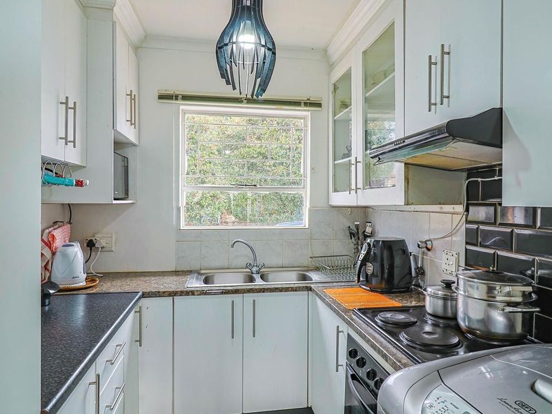 Compact kitchen featuring white cabinetry, dark tiled backsplash, laminate countertops, and integrated cooking appliances, offering a functional layout with natural light.