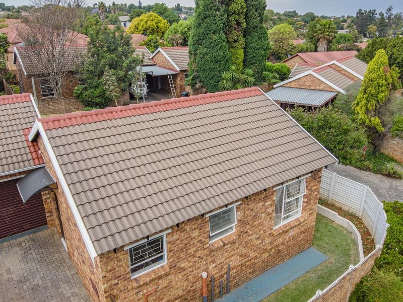 Aerial view of a facebrick townhouse featuring a tiled roof, paved driveway, and secure garage access within a residential complex.