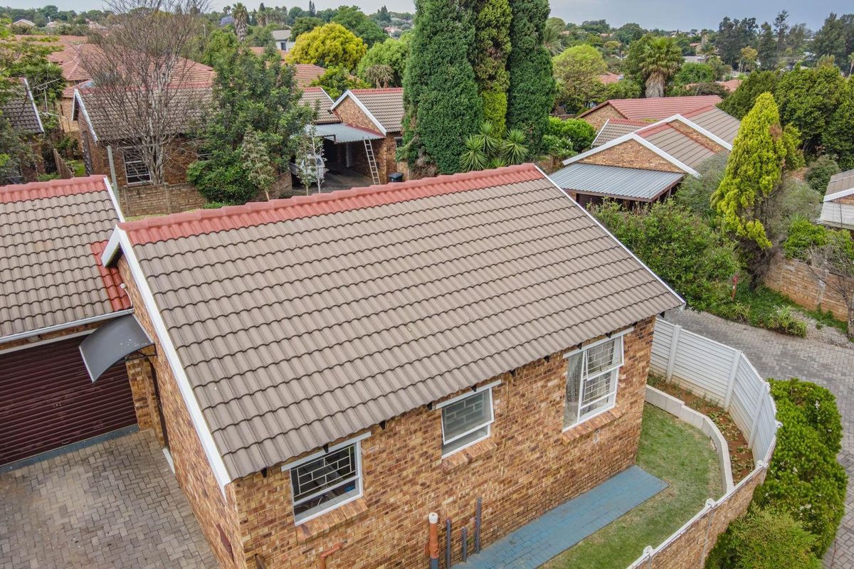 Aerial view of a facebrick townhouse featuring a tiled roof, paved driveway, and secure garage access within a residential complex.