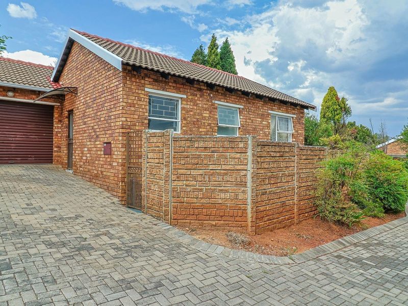 Front exterior view of a face-brick townhouse featuring a paved driveway, private garage, and enclosed garden area with established landscaping.