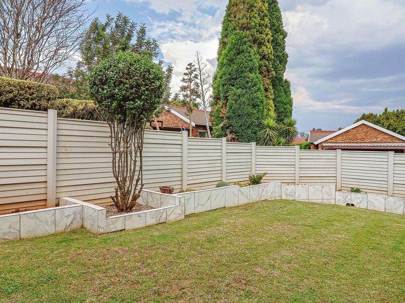 A private rear garden featuring a well-maintained lawn, enclosed by a secure precast concrete boundary wall and decorative tiled planter boxes.