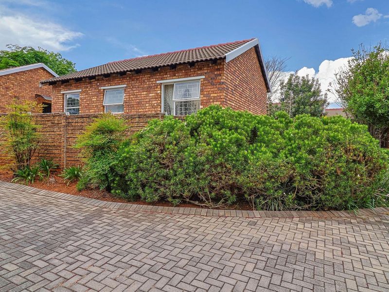 Exterior view of a face brick townhouse featuring a tiled roof, paved driveway, and established garden landscaping.