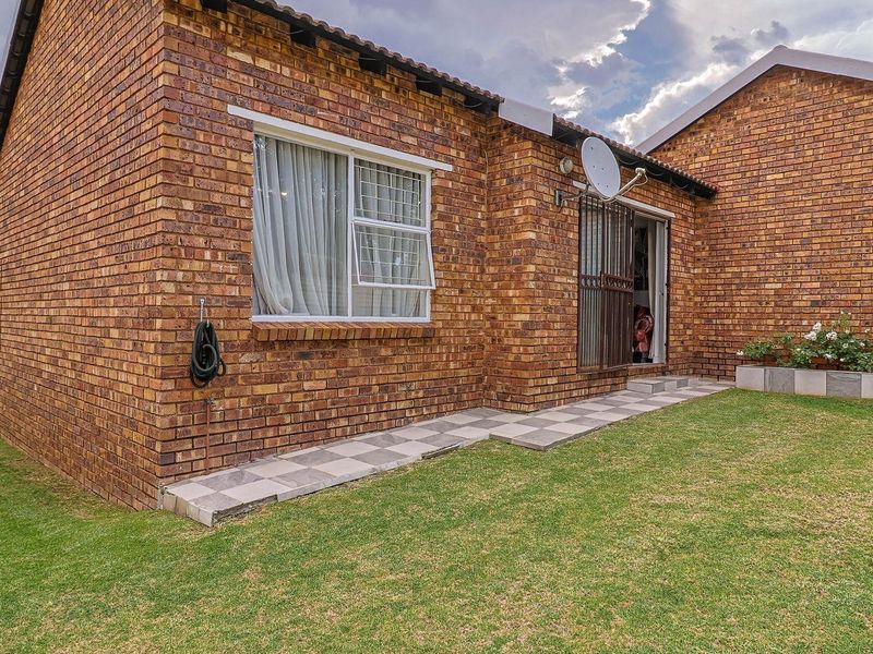 Rear view of a face brick townhouse featuring a small lawn, tiled walkway, and security gate access.