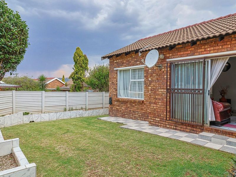 Rear view of the townhouse featuring a face brick facade, tiled roof, paved walkway, and a private garden with raised beds and perimeter fencing.