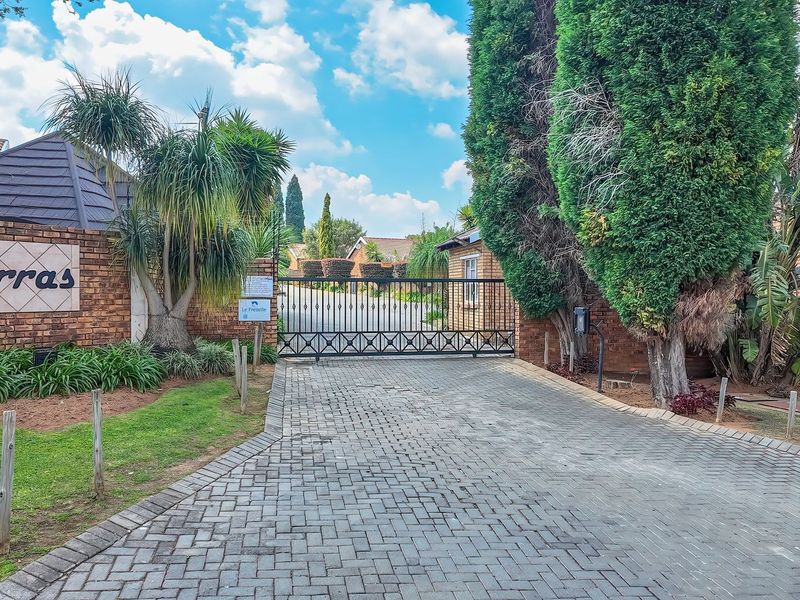 The entrance to Karras townhouse complex featuring a paved driveway, brick boundary wall, and secure metal gate access.