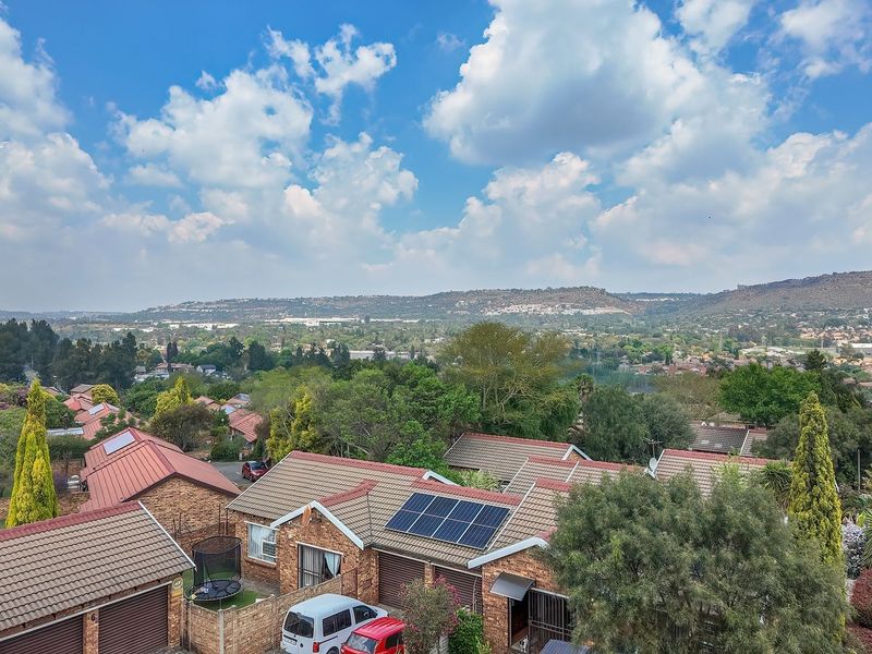 An elevated aerial view of a residential townhouse complex featuring tiled roofs, solar panels, and surrounding suburban landscape.