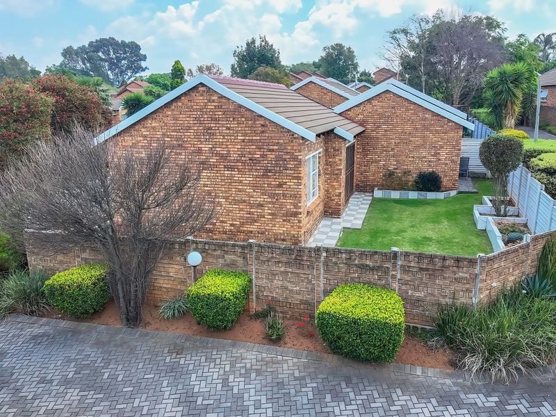 Aerial view of a brick townhouse featuring a private garden, paved driveway, and well-maintained exterior finishes within a residential complex.