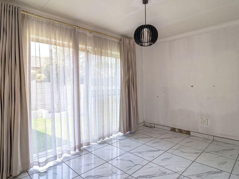 An empty living room featuring marble-look floor tiles, a modern pendant light, and large sliding glass doors leading to the garden.