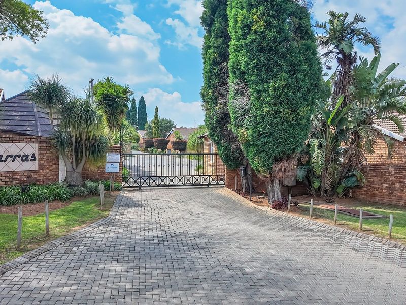 The entrance to Karras complex featuring a secure gated access point, brick paved driveway, and established landscaped gardens.