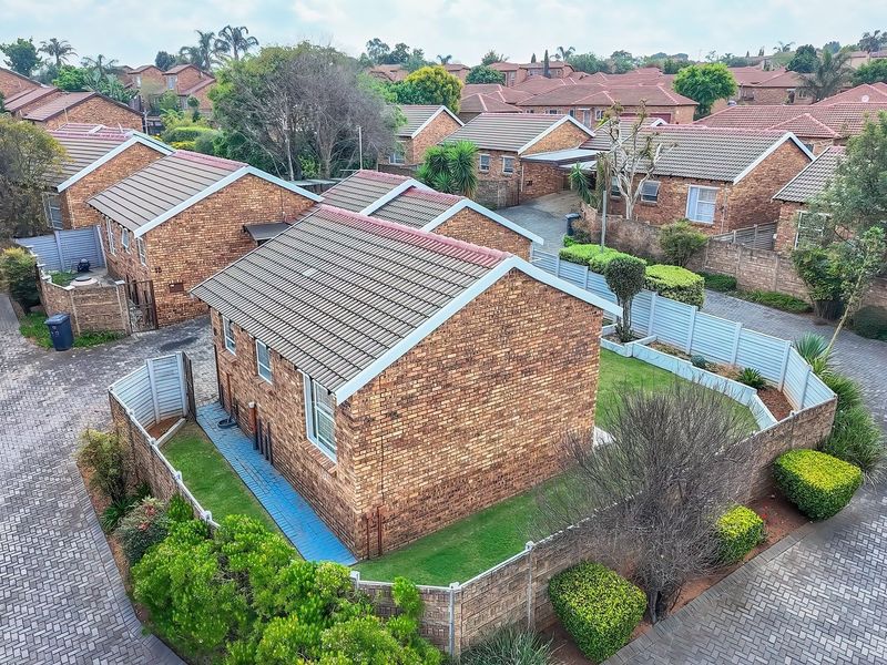 Aerial view of a brick townhouse complex featuring tiled roofs, paved driveways, and private garden areas within a residential estate.